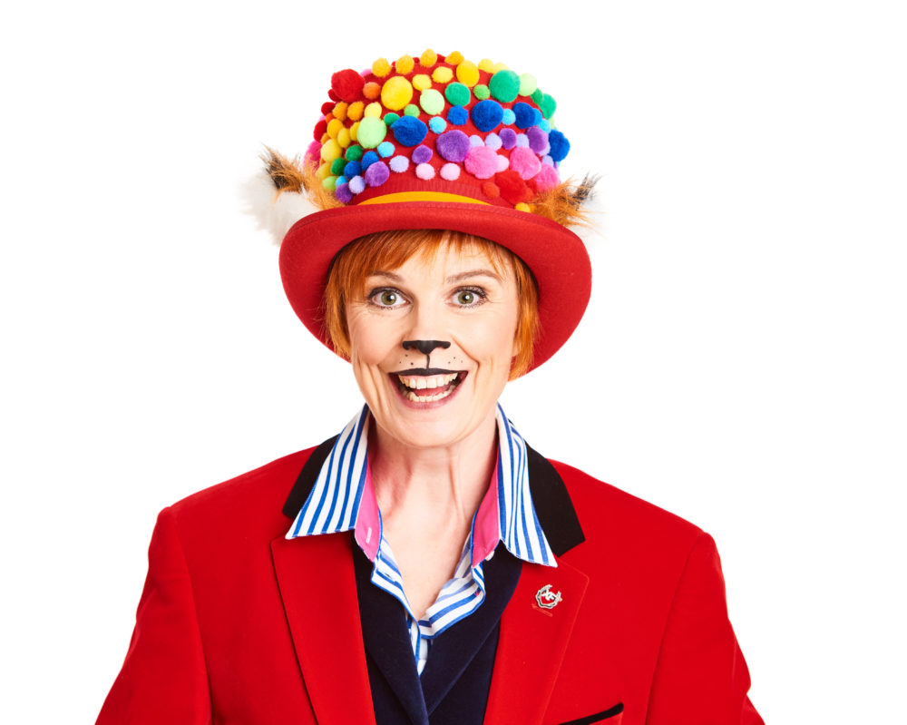 Photo of Louise Wells wearing a bright red jacket and top hat, which has a rainbow of 3D dots swirling around it.